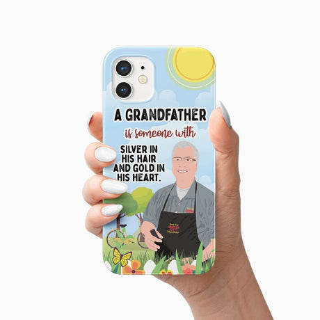 A hand holding a smartphone with a Grandfather Phone Case Personalized from Ecomartists, which includes a heartfelt message about grandfathers and an illustration of an elderly man gardening.