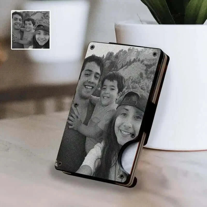 A Personalized Engraved Photo Wallet displaying a personalized black and white photo of three smiling individuals, placed on a surface near a potted plant and a framed picture.